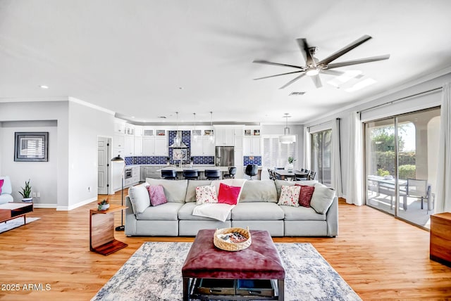 living area featuring ornamental molding, a ceiling fan, light wood-style flooring, and baseboards