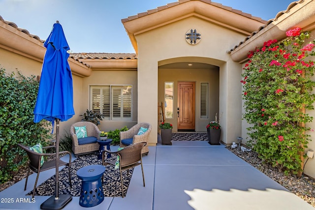 property entrance with a patio area, a tile roof, and stucco siding