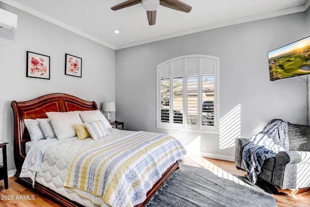 bedroom featuring ceiling fan, wood finished floors, baseboards, a wall mounted air conditioner, and crown molding