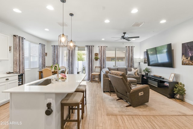 kitchen featuring a breakfast bar, pendant lighting, sink, white cabinets, and a kitchen island with sink