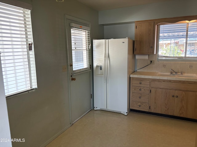 kitchen with plenty of natural light, decorative backsplash, white refrigerator with ice dispenser, and sink