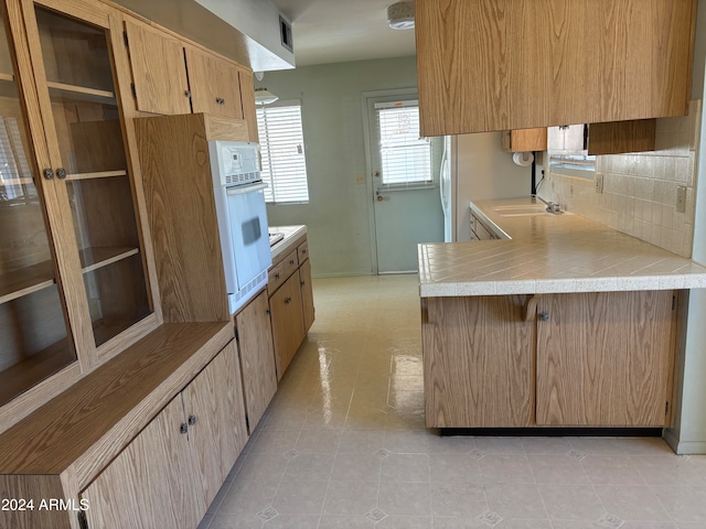 kitchen with oven, sink, light tile patterned floors, tasteful backsplash, and kitchen peninsula