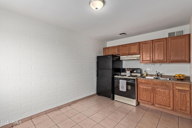 kitchen featuring brick wall, gas range gas stove, light tile patterned flooring, sink, and black fridge