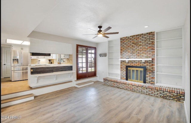 unfurnished living room with a fireplace, ceiling fan, light hardwood / wood-style flooring, and french doors