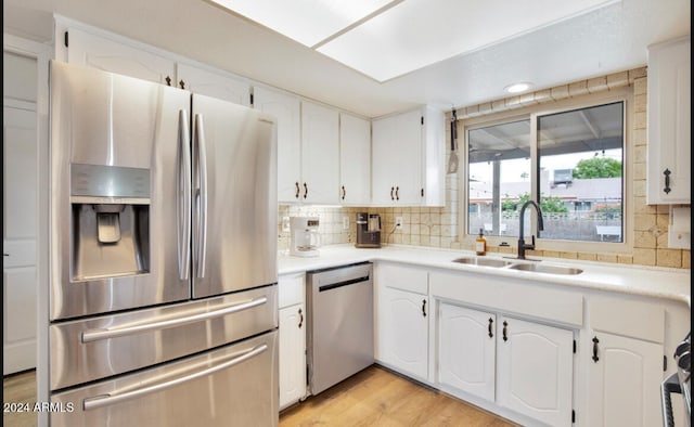 kitchen with backsplash, white cabinets, sink, appliances with stainless steel finishes, and light hardwood / wood-style floors