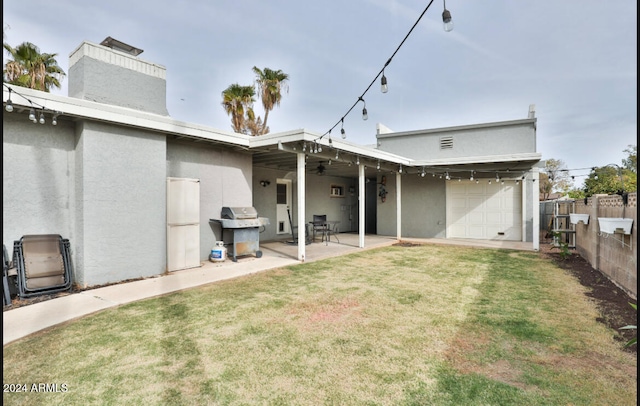 rear view of property featuring a lawn, a garage, and a patio