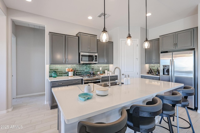 kitchen featuring stainless steel appliances, an island with sink, light countertops, and visible vents