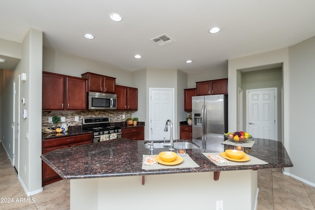 kitchen with decorative backsplash, a kitchen breakfast bar, a kitchen island with sink, sink, and stainless steel appliances