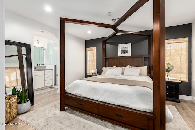 bedroom with light wood-type flooring, visible vents, recessed lighting, connected bathroom, and arched walkways