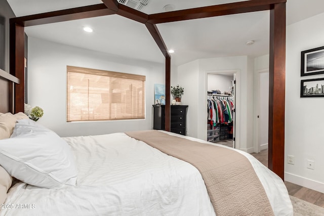 bedroom with wood finished floors, visible vents, baseboards, recessed lighting, and a walk in closet