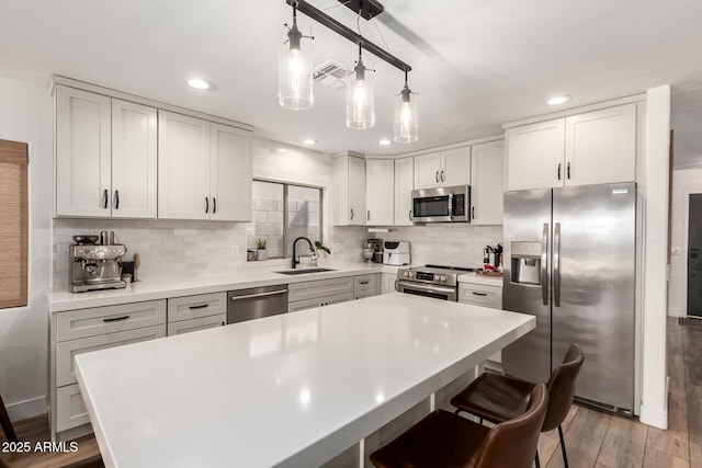 kitchen with wood finished floors, a sink, stainless steel appliances, tasteful backsplash, and a center island