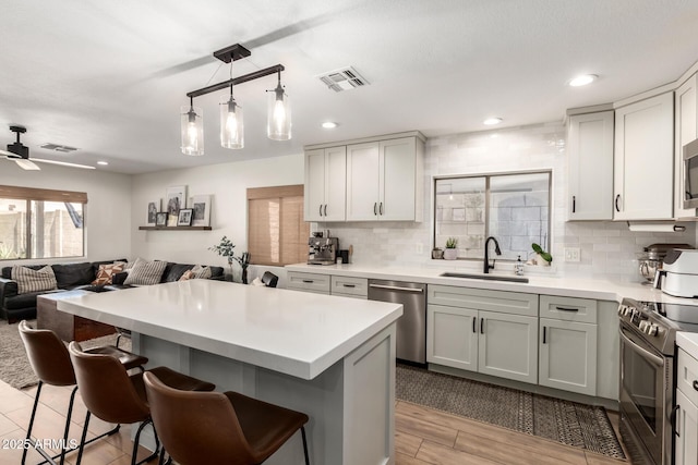 kitchen with visible vents, open floor plan, a kitchen bar, stainless steel appliances, and a sink