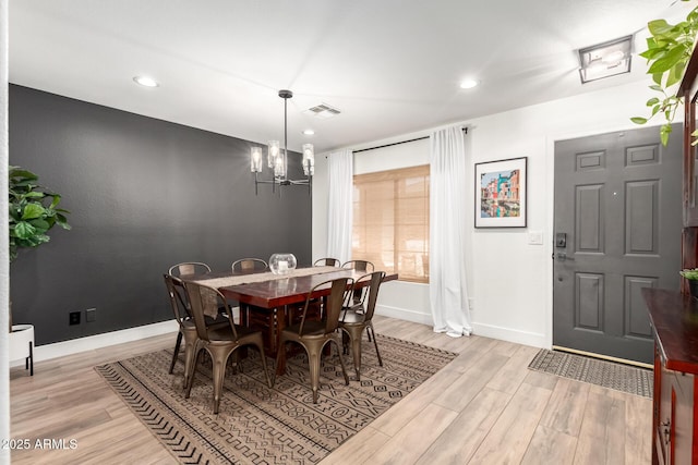 dining area with visible vents, baseboards, light wood-style floors, and an inviting chandelier