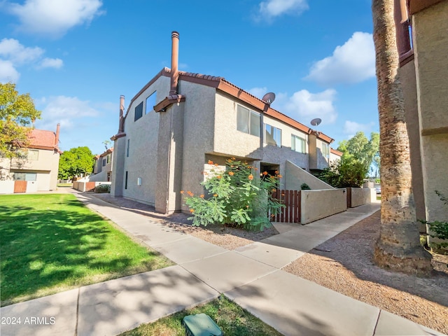 view of property exterior featuring a gate, fence, stucco siding, a tiled roof, and a lawn