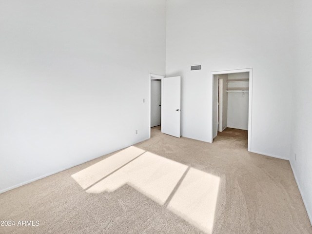 unfurnished bedroom with visible vents, a spacious closet, a closet, a towering ceiling, and light colored carpet