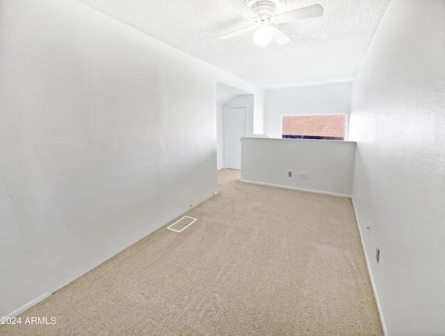 empty room with ceiling fan, light colored carpet, visible vents, and a textured ceiling