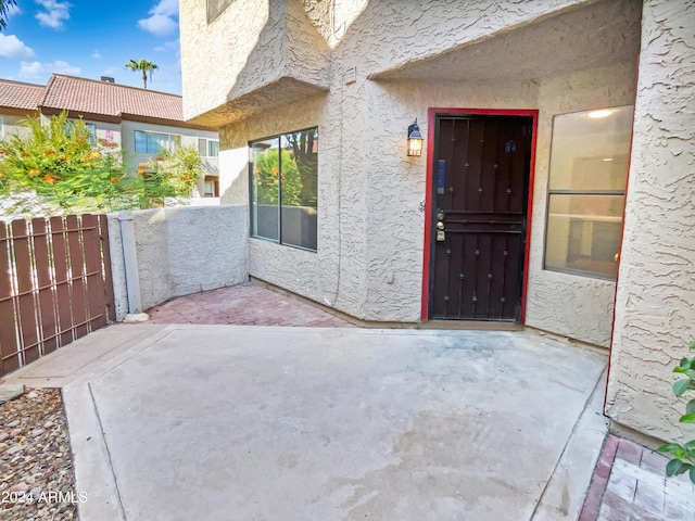 entrance to property featuring stucco siding, a patio area, and fence