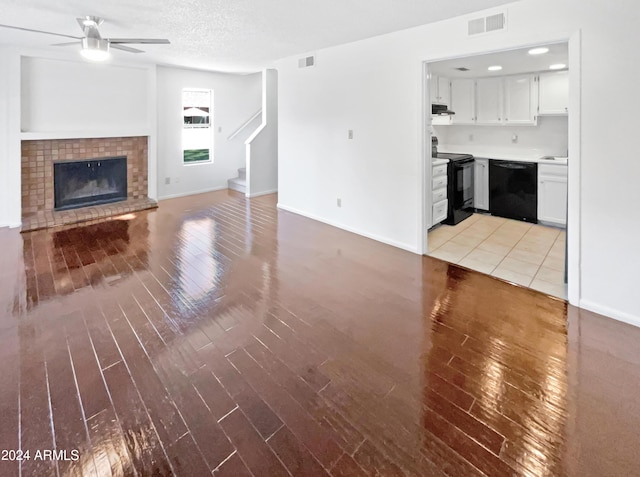 unfurnished living room featuring light wood-type flooring, visible vents, a brick fireplace, and ceiling fan