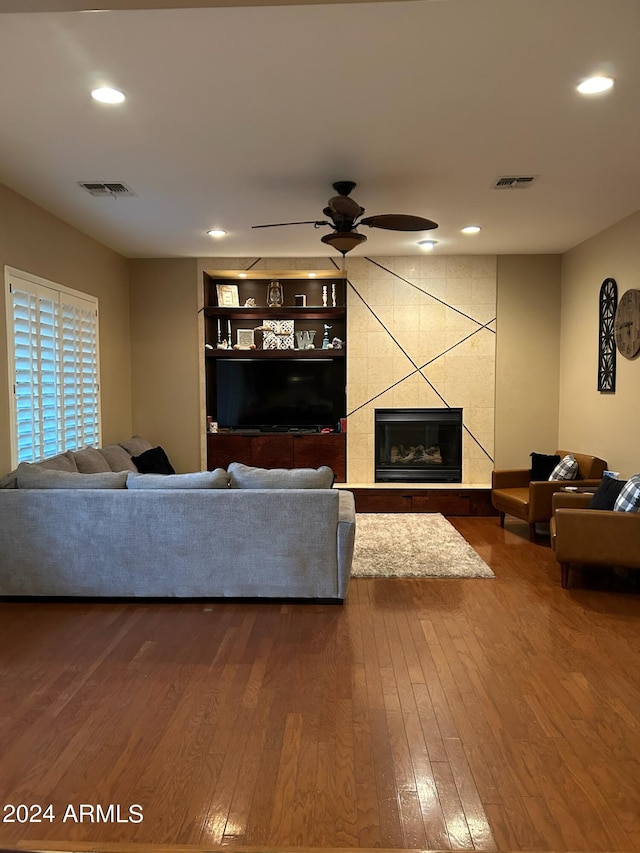 living room with ceiling fan, wood-type flooring, and a tile fireplace