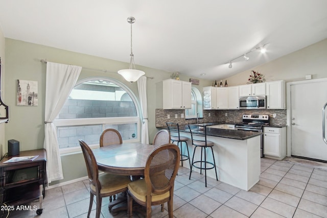 kitchen featuring lofted ceiling, stainless steel appliances, decorative light fixtures, and white cabinetry