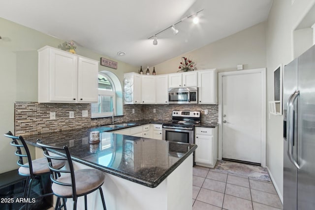 kitchen featuring kitchen peninsula, tasteful backsplash, lofted ceiling, white cabinets, and appliances with stainless steel finishes