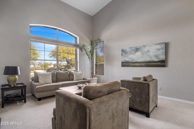 living area featuring a high ceiling, baseboards, and light carpet