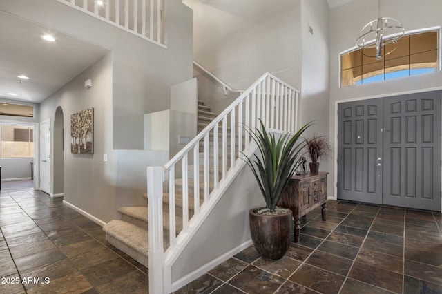 entrance foyer with stone tile floors, stairway, arched walkways, a high ceiling, and baseboards