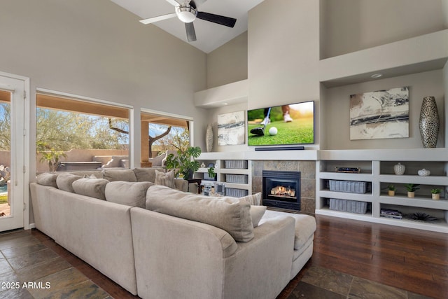 living area with a tile fireplace, high vaulted ceiling, dark wood-type flooring, and a ceiling fan