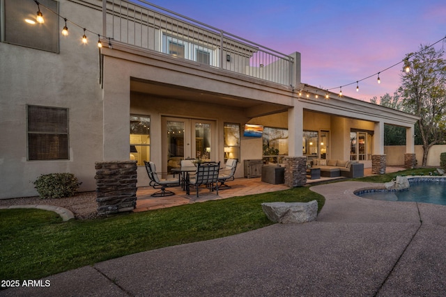 back of house at dusk featuring stucco siding, french doors, and a patio