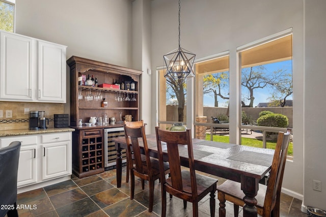dining space with wine cooler, a notable chandelier, plenty of natural light, and a high ceiling