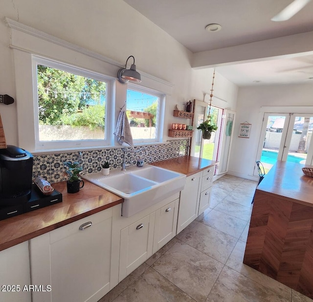 kitchen featuring butcher block countertops, backsplash, white cabinets, and a sink