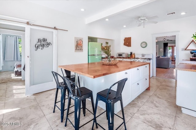 kitchen featuring a wealth of natural light, white cabinets, wooden counters, and freestanding refrigerator