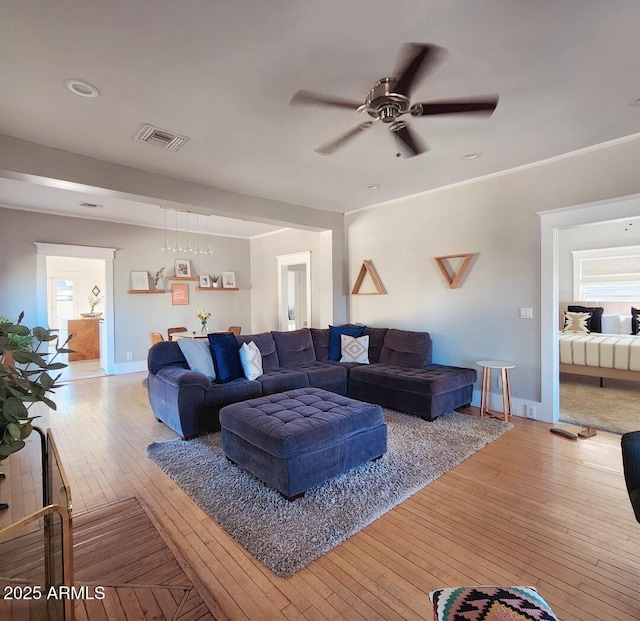 living room featuring baseboards, visible vents, light wood finished floors, ornamental molding, and ceiling fan