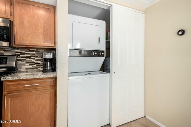 washroom featuring laundry area, stacked washing maching and dryer, and baseboards