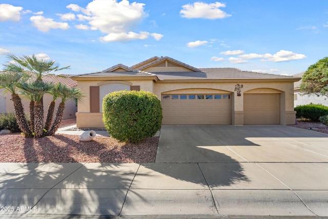 view of front of home featuring an attached garage, a tiled roof, concrete driveway, and stucco siding