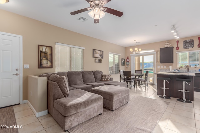 tiled living room with ceiling fan with notable chandelier