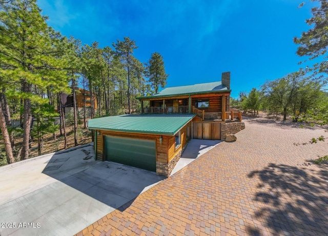 view of front of house with a chimney, metal roof, concrete driveway, and stone siding