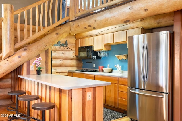 kitchen featuring black microwave, a peninsula, light countertops, freestanding refrigerator, and log walls