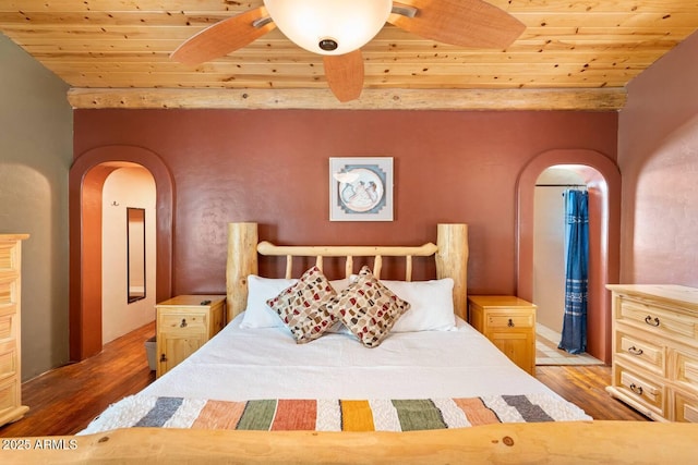 bedroom featuring beam ceiling, wood finished floors, arched walkways, and wooden ceiling