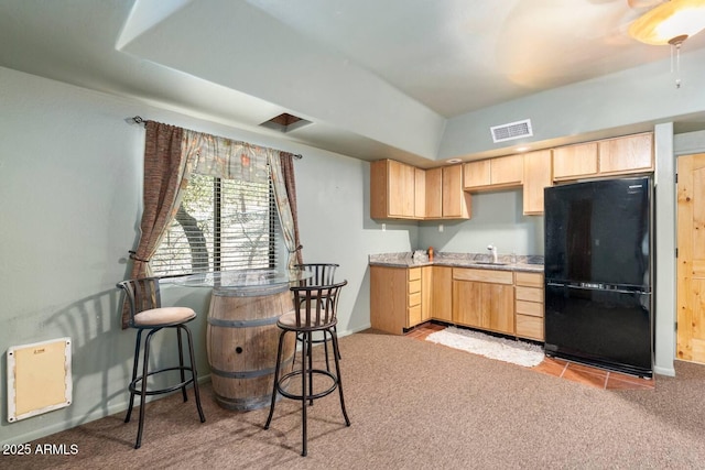 kitchen featuring a sink, visible vents, light brown cabinets, freestanding refrigerator, and light carpet