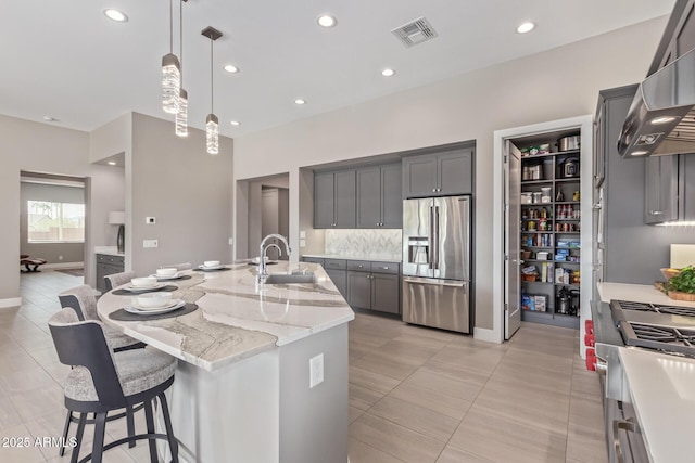 kitchen with wall chimney exhaust hood, sink, gray cabinetry, a center island with sink, and stainless steel appliances