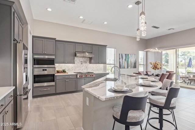 kitchen with sink, a breakfast bar area, stainless steel appliances, tasteful backsplash, and decorative light fixtures