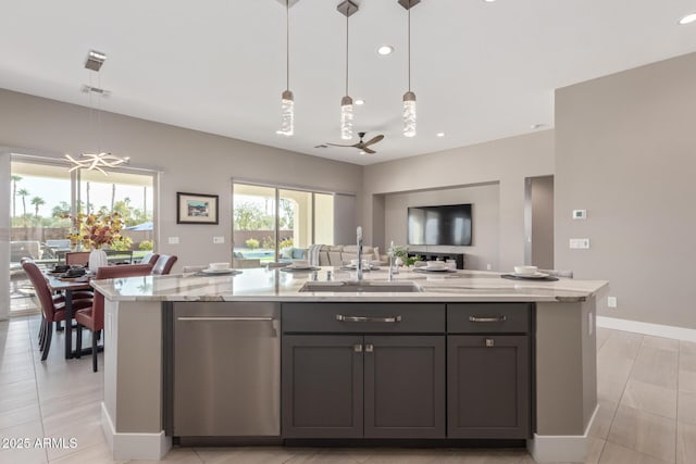 kitchen featuring sink, ceiling fan with notable chandelier, light stone counters, an island with sink, and decorative light fixtures