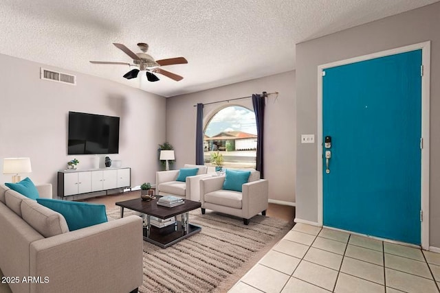 living area featuring visible vents, a ceiling fan, light tile patterned floors, and a textured ceiling