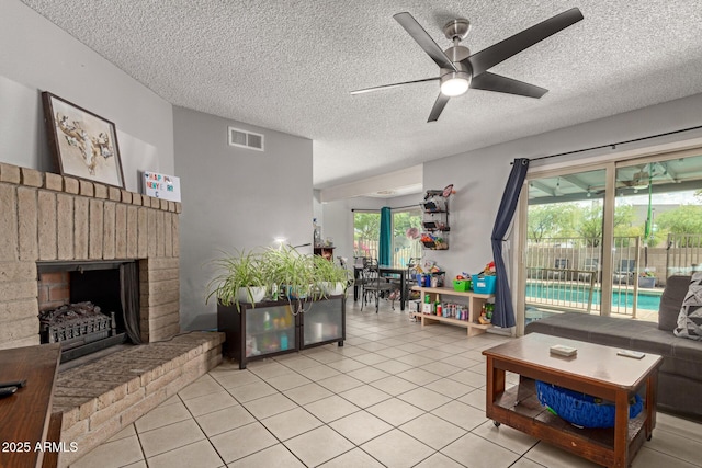 living room with light tile patterned floors, a fireplace, a textured ceiling, a ceiling fan, and visible vents