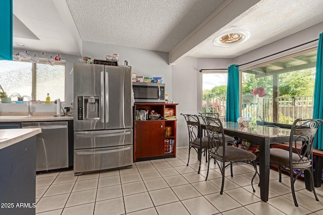 kitchen with a textured ceiling, light countertops, light tile patterned flooring, appliances with stainless steel finishes, and a sink