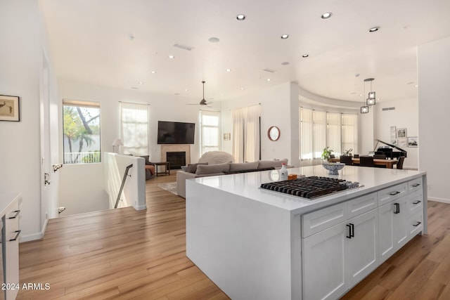 kitchen featuring hanging light fixtures, a center island, light hardwood / wood-style floors, stainless steel gas cooktop, and white cabinets