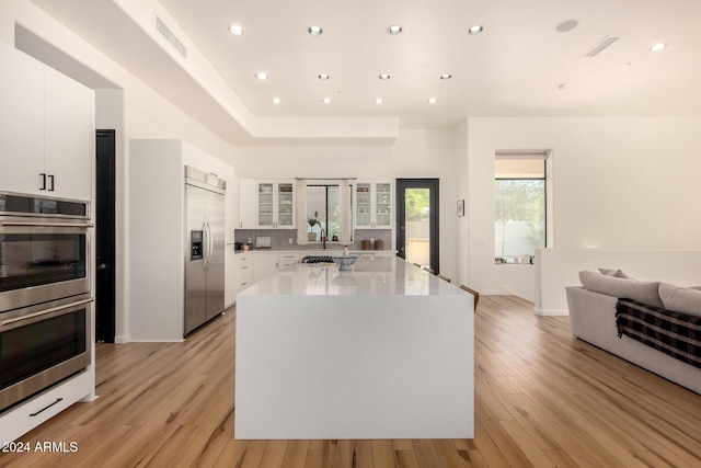 kitchen featuring a center island, appliances with stainless steel finishes, light hardwood / wood-style floors, decorative backsplash, and white cabinets