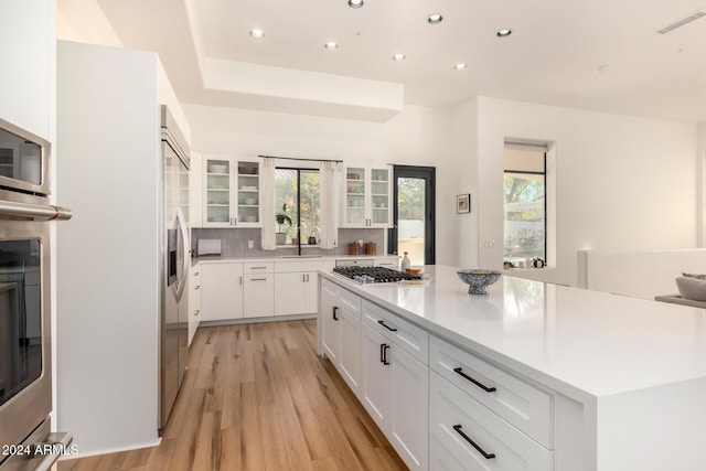 kitchen featuring white cabinetry, tasteful backsplash, a center island, stainless steel appliances, and light hardwood / wood-style floors