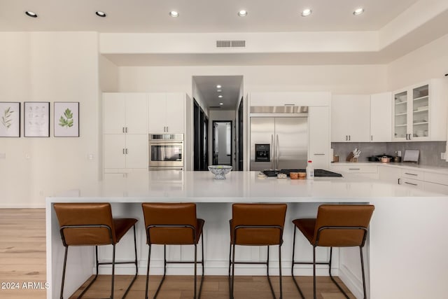 kitchen with white cabinetry, light wood-type flooring, a kitchen breakfast bar, stainless steel appliances, and backsplash